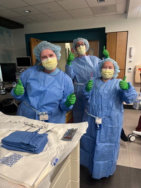 three resdients in surgical gear give two thumbs up from an operating room